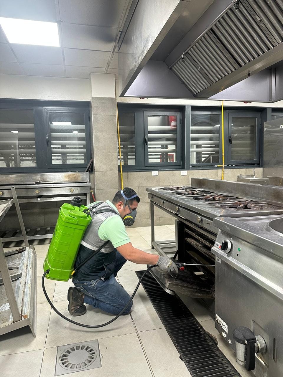 Técnico aplicando tratamiento bajo la cocina industrial de un local
