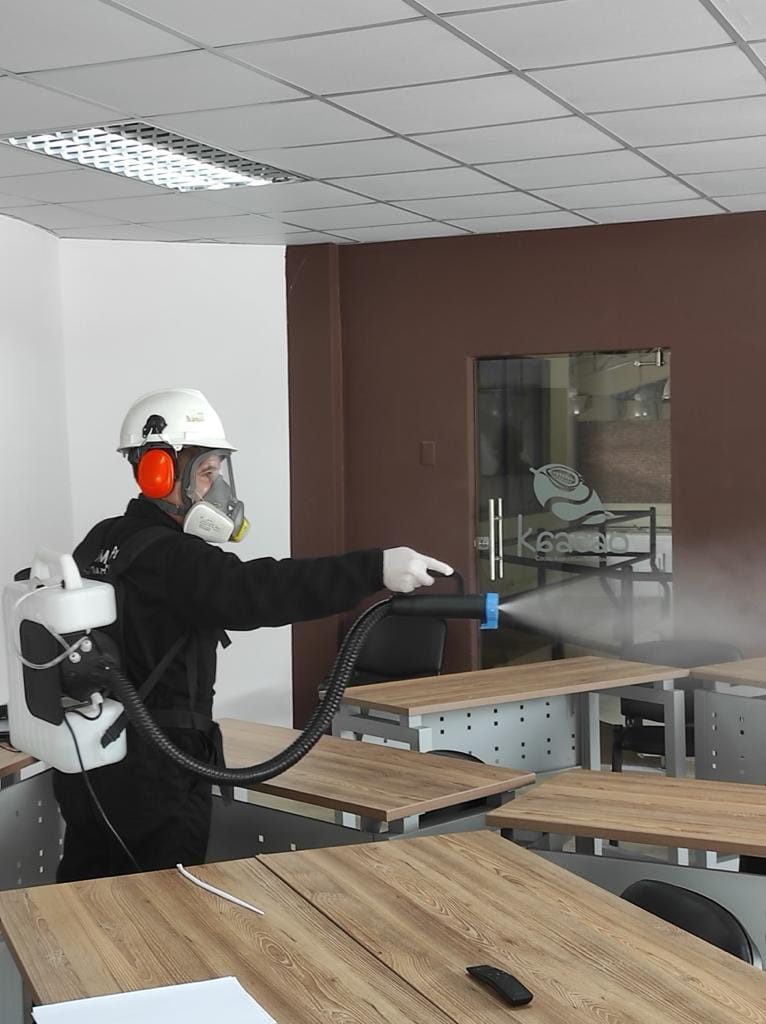 Técnico con equipo de protección desinfectando una sala de reuniones